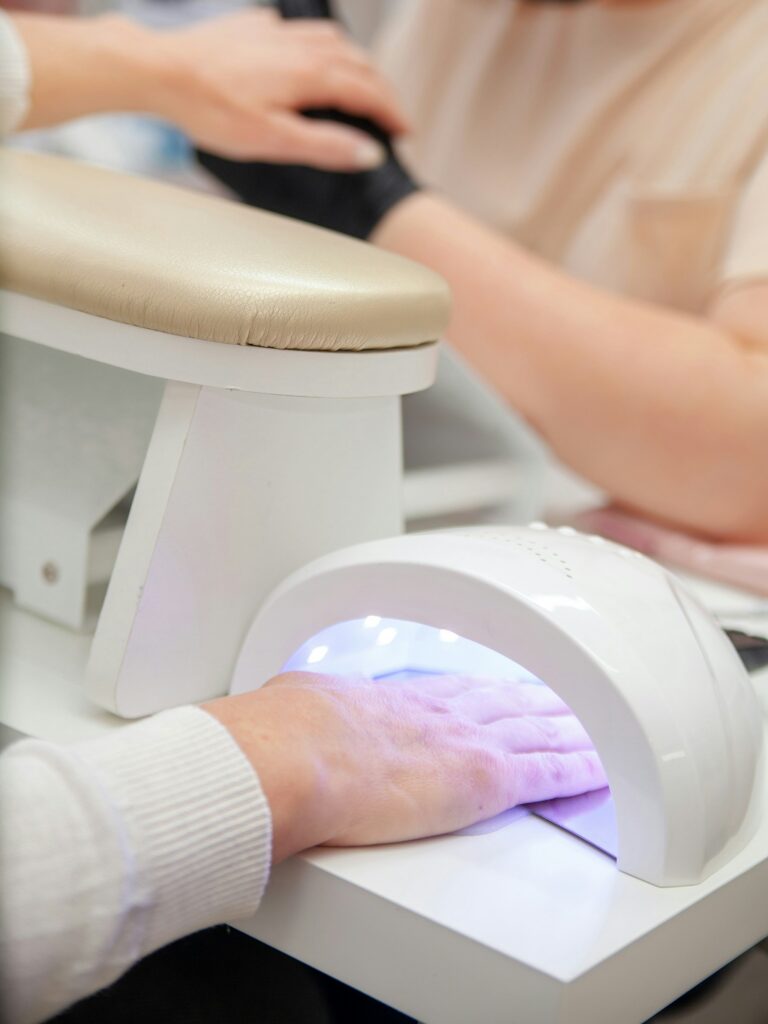 Klientė nagų salone kietina BIAB manikiūrą po UV lempa