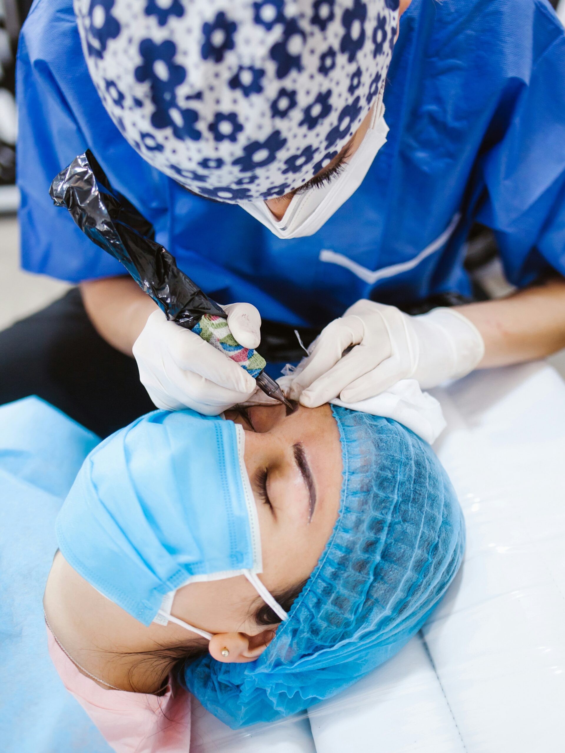 Artimas moters, kuriai meistrė atlieka microblading procedūrą, vaizdas – ji guli ant procedūrinės lovos ir dėvi kaukę