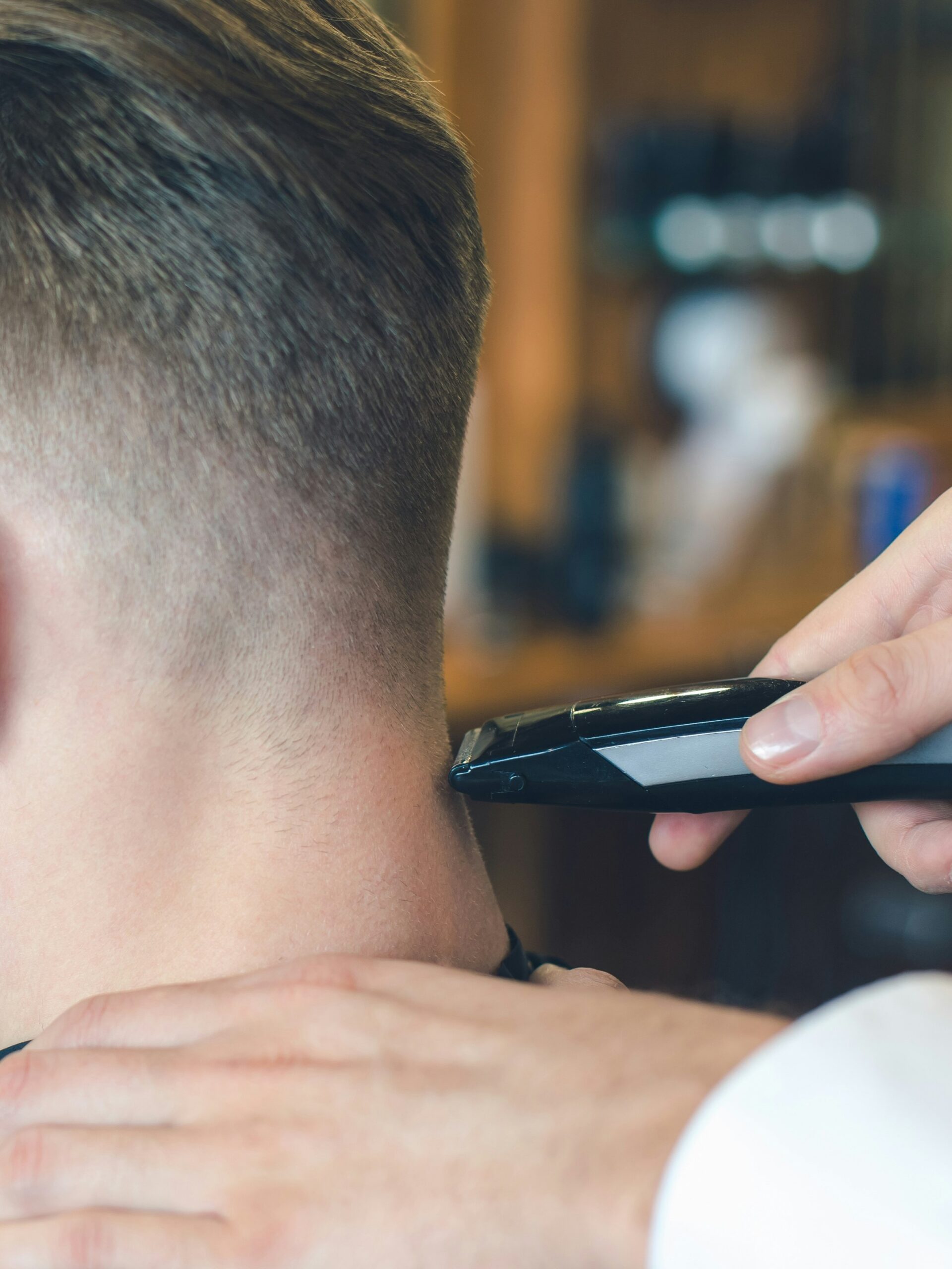 Artimas vaizdas: barberis mašinėle kirpdamas taper fade klientui su tiesiais plaukais pakaušio srityje