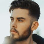 Vyras lauke su tamsiais plaukais ir taper fade kirpimu su tekstūruota vir&scaron;utine dalimi