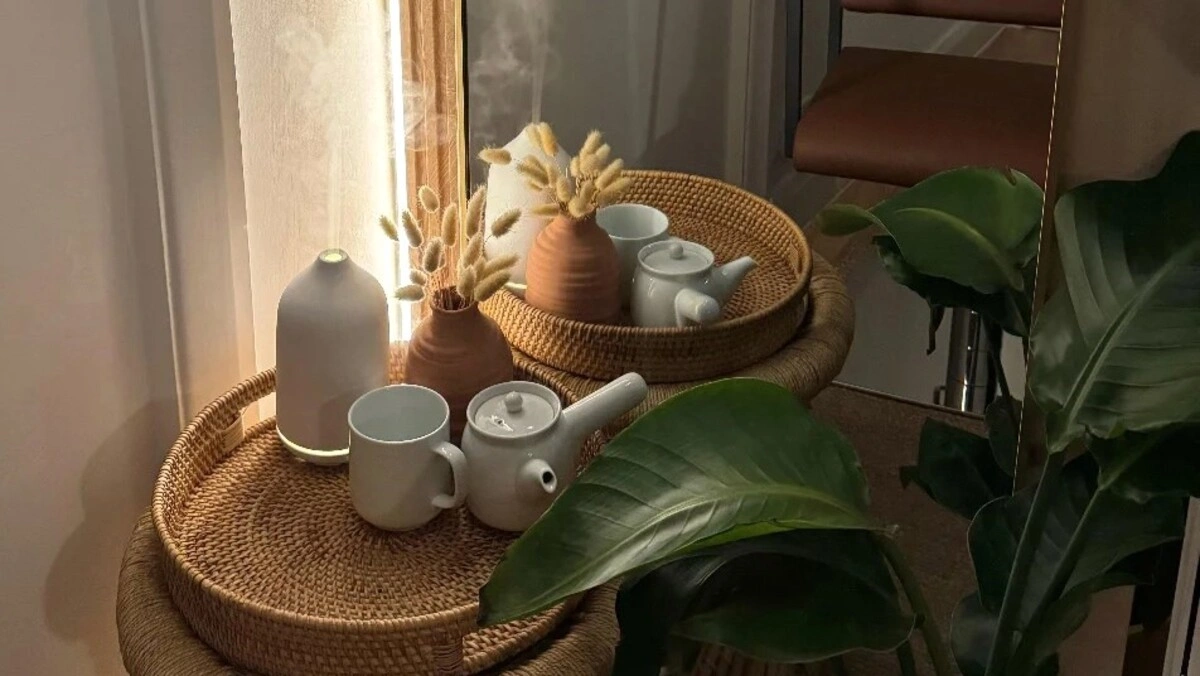 Vytelių padėklas iš arti su aromato difuzoriumi ir arbatos rinkiniu šalia didelio žalio augalo salone