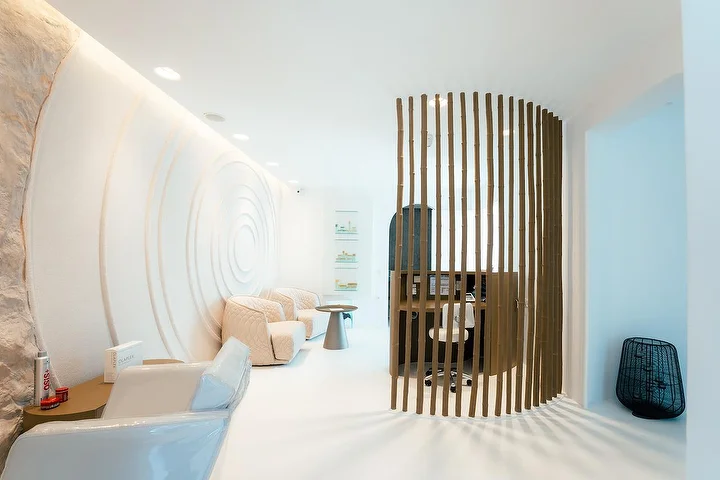 Rami, urvą primenanti SPA erdvė su išlenktomis baltomis sienomis, viena jų išraižyta koncentriškomis bangelėmis, su švelniu netiesioginiu apšvietimu, minkštais kreminės spalvos foteliais ir išlenkta medinių lentelių pertvara, atskiriančia ramų procedūrų kampelį.