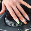 Ranka su electric mani, padėta ant Pioneer DJ grotuvo jog wheel, su neoniniais french tips gyvūnų ra&scaron;tu ir spiralėmis