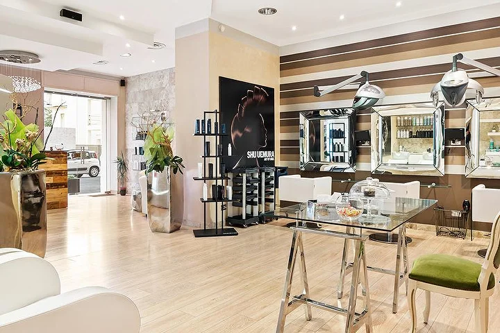 Elegantiškos styling vietos Hair Queen salone Cagliari mieste su kreminių ir rudų juostų sienomis ir aukštais sidabro spalvos vazonais.
